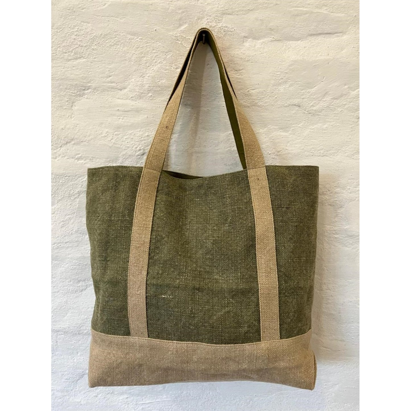Green tote bag with brown handles on a light stone background