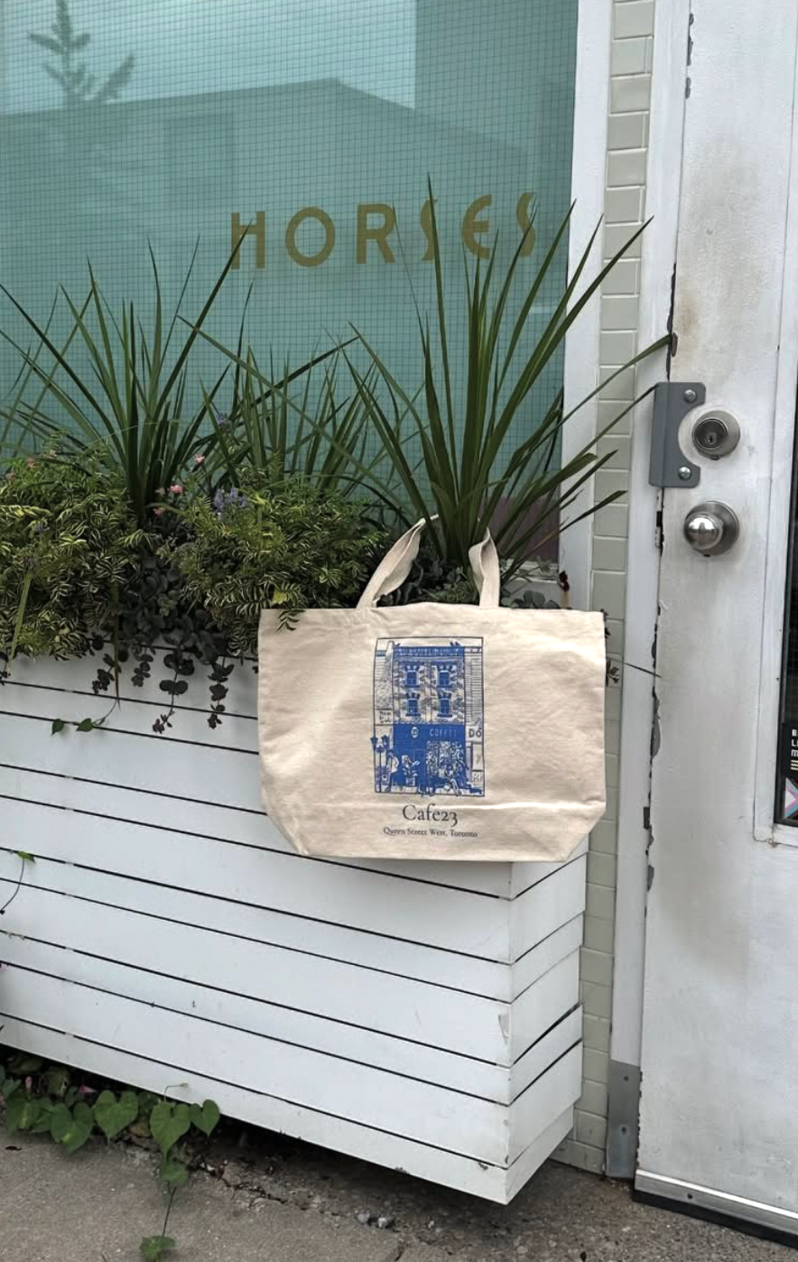 Beige tote bag with blue design hanging on a white door with glass panels